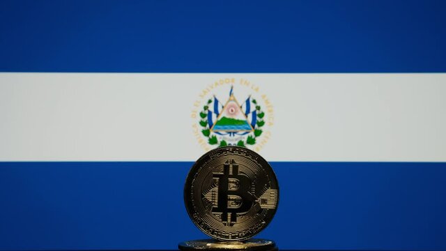 Bitcoin representation coin placed in front of blurred Salvador's national flag. El Salvador is the first country to adopt bitcoin as legal tender. Concept.