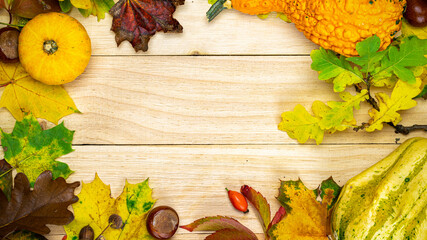 Flat lay autumn. Natural harvest with orange pumpkin, fall dried leaves, red berries and acorns, chestnuts on wooden background in shape frame. For seasonal offers and holiday post card, top view.