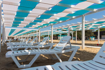 Anapa. Krasnodar Territory - May 14, 2021: canopies, gazebos painted in blue and white stripes, architectural structures made of wood and white sun beds on the Black Sea beach
