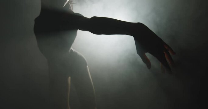 Modern ballet performance. Silhouette of graceful ballerina dancing mysterious dance in textured smoke in spotlight