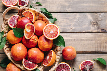 Pile of blood oranges in a basket on a wooden table background. Flat lay, top view, copy space