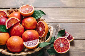 Whole and sliced blood oranges in a basket on wooden table background. Close up, copy space