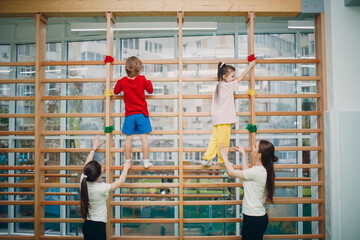 Kids at Swedish wall exercises in gym at kindergarten or elementary school with teachers. Children sport and fitness concept