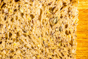 Slice of rustic natural yeast-free bread with flax, poppy seeds, sesame seeds, millet, pumpkin and sunflower seeds, on a wooden board, black background, hard light, photo in a low key, close up.