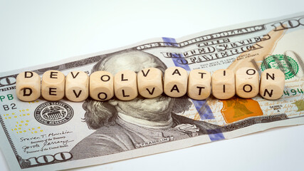 The word devolvation on wooden cubes located on a hundred dollar bill