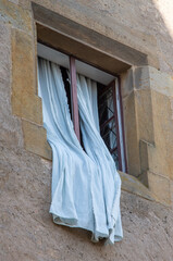 White curtains hang from a window in an old sandstone building