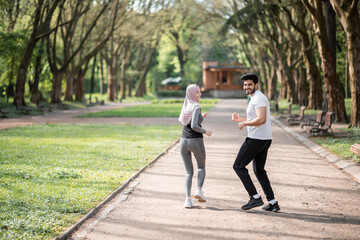 Happy arabian couple in active wear jogging at green park during morning time. Young man and woman...