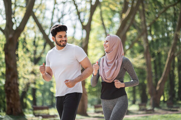 Healthy sport couple in active clothes enjoying morning run at green park. Muslim man and woman in...