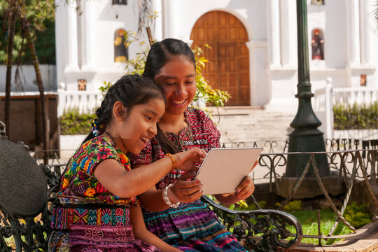 Image of happy indigenous girls outdoors in the park using a laptop.