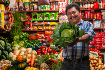 A salesman showing a cabbage in his hands is in a grocery store.
