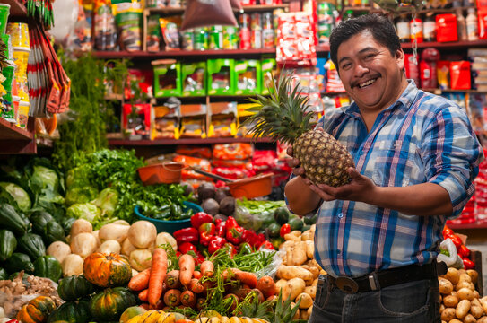 Seller holding a pineapple, in his grocery store.