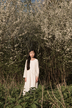Asian girl in white dress standing in front of bush in bloom in spring