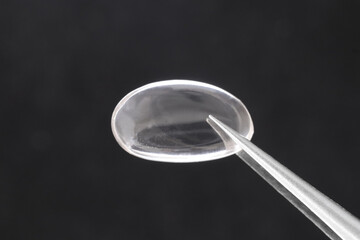 Smoky quartz jewel stone texture in tweezers on black background. Macro closeup.