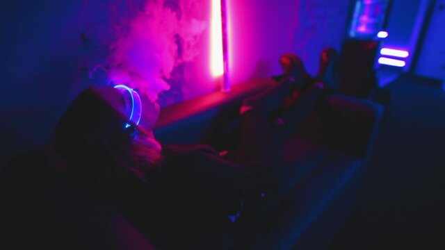 Vape steam and neon noir. Young woman smokes an electric cigarette. 