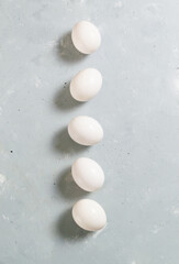 Five white chicken eggs lie on a gray background.