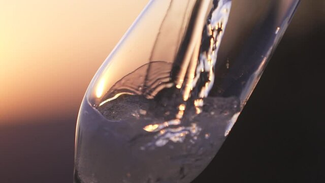 Close-up of a tall glass filled with champagne, wine, against the background of sunset, dawn. Slow motion. 120 fps.