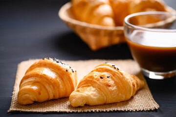 French croissant with black sesame seeds and coffee cup on black background, morning breakfast