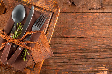 Spoon, fork and knife, restaurant cutlery, on a brown linen napkin, on rustic wooden background