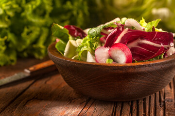 Fresh and healthy seasonal vegetable salad with lettuce, radishes, onion and butter salad with seasonal spices and olive oil, in a wooden bowl on a rustic background.
