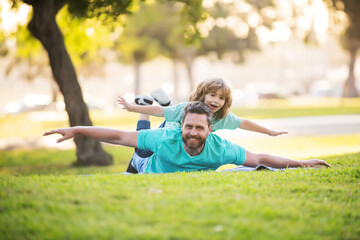 Father lying on grass, with excited happy little child son on shoulder. Carefree two man generations family having fun. Weekend man family concept.