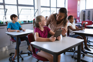 African american female teacher teaching caucasian girl to use digital tablet in the class at school