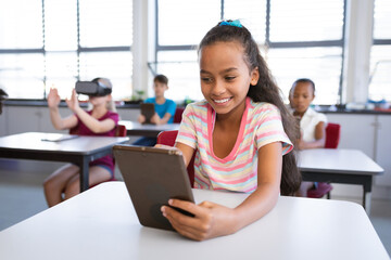 Smiling african american girl using digital tablet while sitting on her desk in class at school