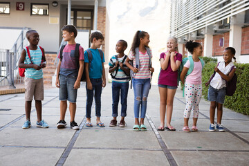 Group of diverse students with backpacks smiling while looking at each other at school