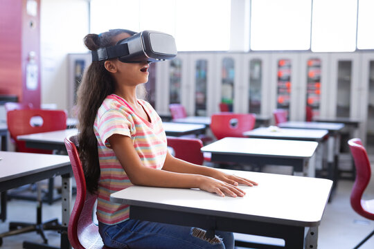 African american girl wearing vr headset while sitting on her desk in the class at school