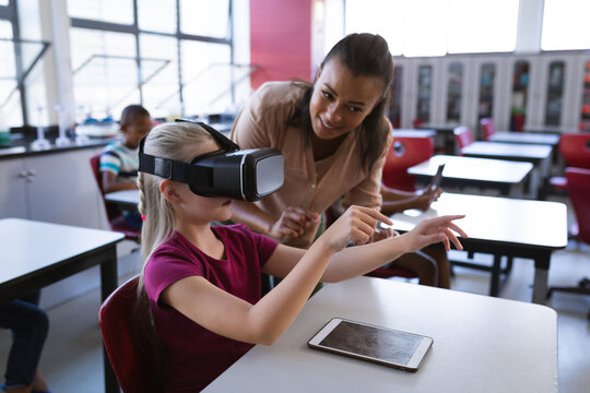 African american female teacher teaching caucasian girl to use vr headset in the class at school