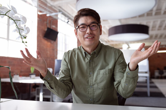 Happy asian businessman sitting at desk talking and gesturing during video call