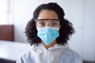 Portrait of african american female cleaner wearing ppe suit, glasses and mask in office