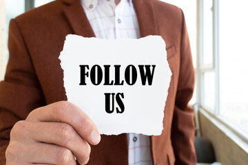 Businessman holds a card with the word follow us. Business or social media concept.