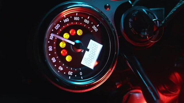 Motorcyclist turns on ignition of modern classic motorcycle. Arrows and indicators on speedometer dashboard. Close-up view.