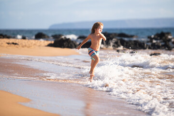 Child running through water close to shore along the sea beach. A boy runs along the sea coast. Rest of children on summer vacation.