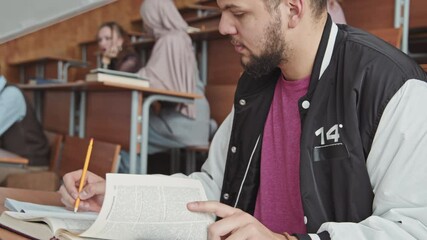 Tilt-up medium slowmo of bearded male university student sitting at desk in lecture hall using smartphone for cheating during exam - Powered by Adobe