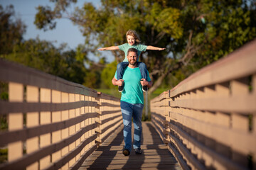 Father giving son ride on back in park. Portrait of happy father giving son piggyback ride on his shoulders. Cute boy with dad outdoor.