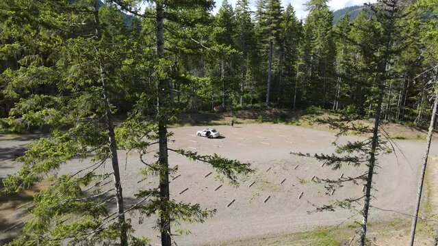 Man And Silver Car In Parking Lot Flying Backwards Through Green Trees Reveal Natural Lake Mountain Clouds Aerial Drone Shot In Lake Cushman Hoodsport Mason County Washington State Pacific Northwest