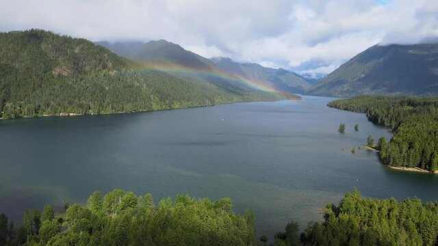 Natural rainbow over lush rainforest green tree mountain hills valley with blue water on cloudy sunny day aerial drone shot in Lake Cushman Hoodsport Mason County Washington State Pacific Northwest