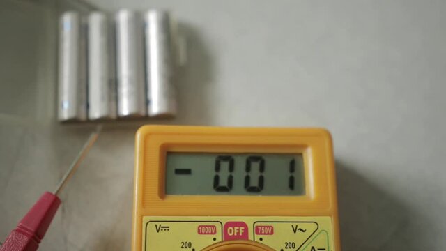 A person measuring the voltage of AAA batteries using a multimeter for checking if they are fully charged