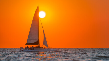 Fototapeta premium Sailboat. Beautiful seascape with sail boat or luxury yacht on horizon. Ocean sunset and red sky. Summer vacation in Florida. Good for travel agency, billboard or post card. Photo with copy space.
