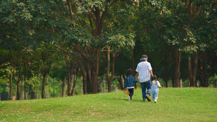 grand father holding hands of grandchildren walking together in park