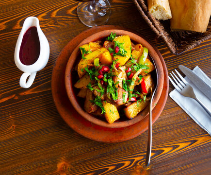 Traditional georgian family dish Ojakhuri - roast of meat and potatoes with onion, spices, fresh greens and pomegranate seeds served in earthenware ketsi pan