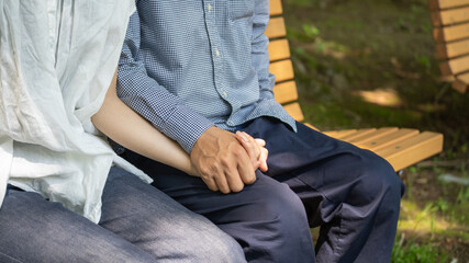 公園のベンチで手を繋ぐカップル。