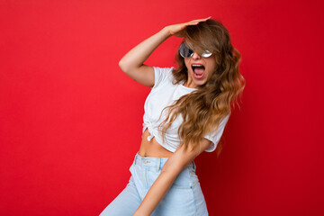Attractive happy joyful young blonde woman wearing everyday stylish clothes and modern sunglasses isolated on colorful background wall looking at camera