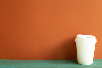 Disposable white paper coffee cup on green wooden table. red wall background