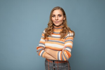 Young charming fascinating sexy self-confident blonde woman wearing casual striped pullover isolated over blue background with free space and crosses hands