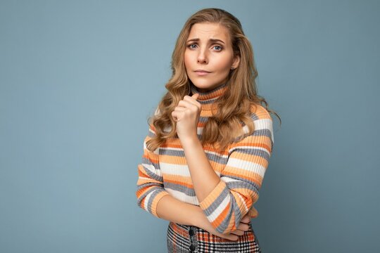 Photo shot portrait of young nice winsome beautiful sad upset thoughtful blonde woman with sincere emotions wearing striped sweater isolated over blue background with free space and thinking with