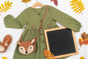 Stylish autumn set of child clothes. Green dress, brown bag, shoes, letter board frame and autumn...