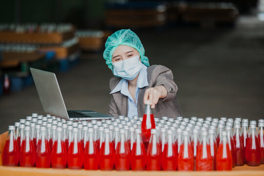 Female Inventory Manager with labtop is checking juice bottles before shipment. Inspection quality control. Manager inspecting production line at drinks production factory - Powered by Adobe