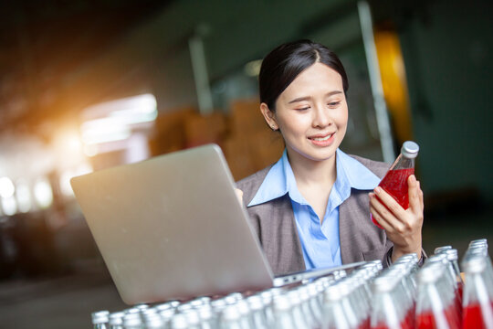 Female Inventory Manager with labtop is checking juice bottles before shipment. Inspection quality control. Manager inspecting production line at drinks production factory